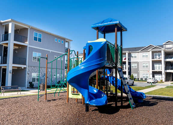 A playground with a blue slide in front of apartment buildings.