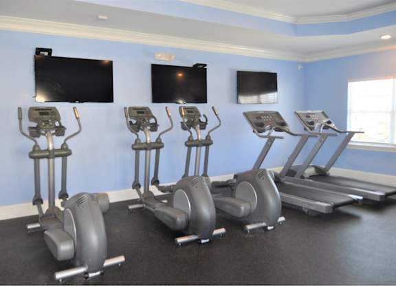 A gym with a row of exercise bikes and two flat screen TVs on the wall.