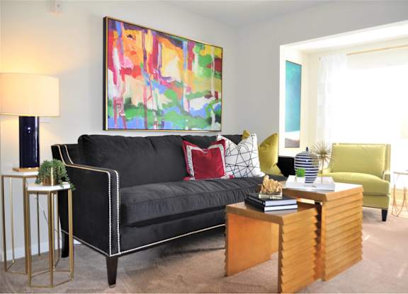 A living room with a black couch, a green chair, and a painting on the wall.