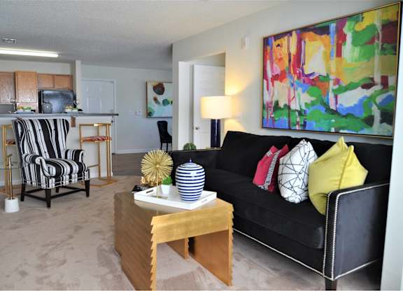 A living room with a black couch and a painting on the wall.