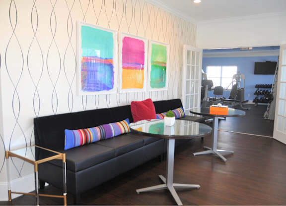 A black couch with colorful pillows sits in front of a wall with three colorful paintings.