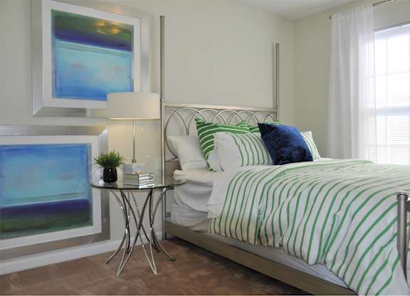 A bedroom with a bed, nightstand, and a painting on the wall.