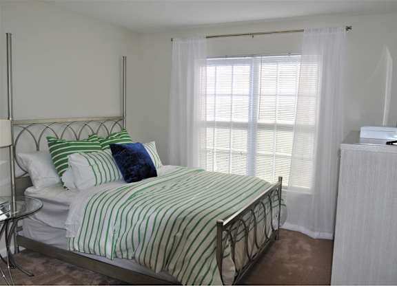 A bed with a green and white striped comforter sits in a room with a window.