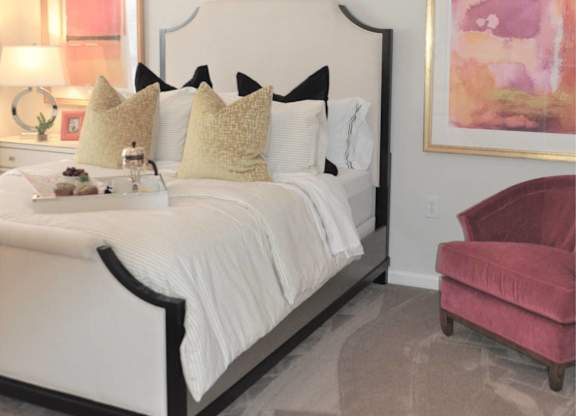 A bedroom with a white bed and a pink chair.
