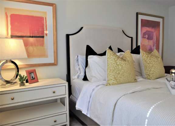 A white bed with a white headboard and a white nightstand with a lamp and a picture frame on it.