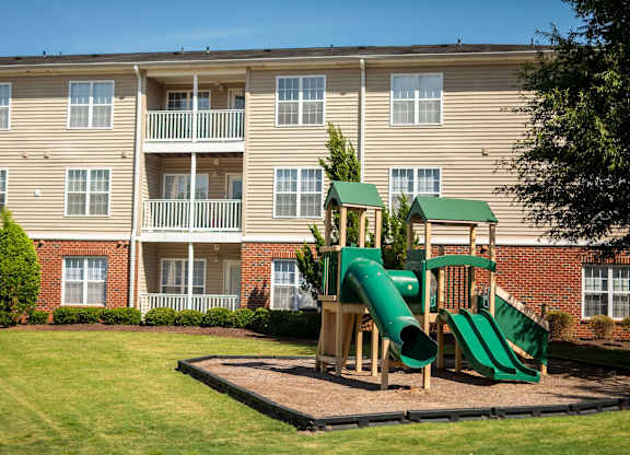 A playground with a green slide in front of a building.