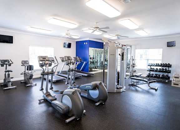 A gym with a variety of exercise equipment including treadmills, stationary bikes, and weight machines.
