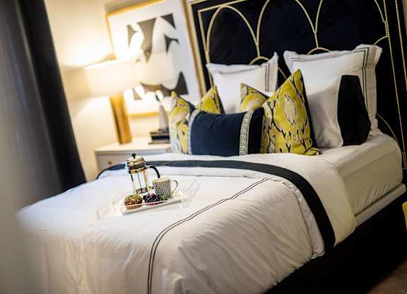 A bed with white sheets and a tray with a bottle and glasses on it.