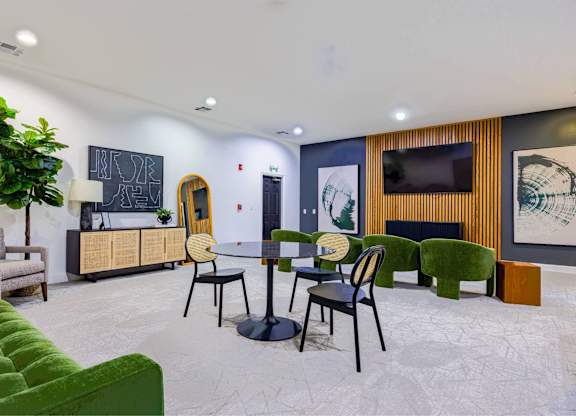 A room with a green couch, a table with chairs, and a plant.