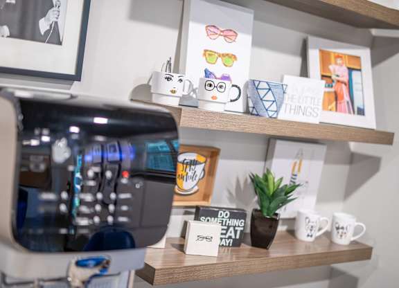 A coffee machine is on the left with a shelf above it holding a sign that says "Do something nice today" and a small potted plant.