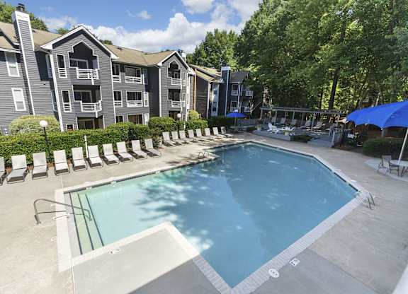 A swimming pool surrounded by lounge chairs and umbrellas in front of apartment buildings.