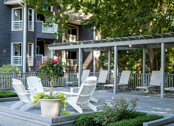 A patio with white chairs and a table with a potted plant on it.