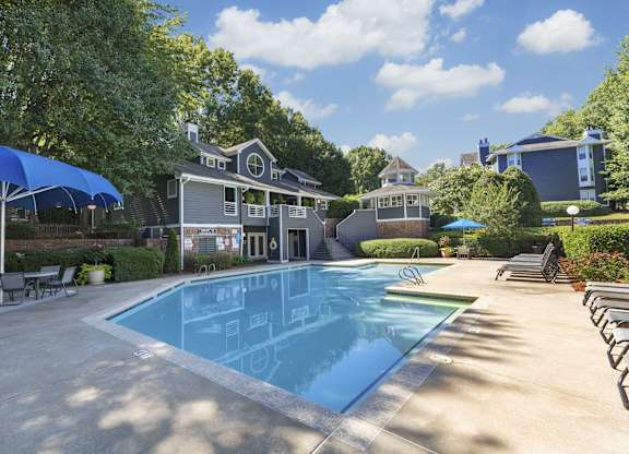 A large swimming pool in front of a house with a blue umbrella.
