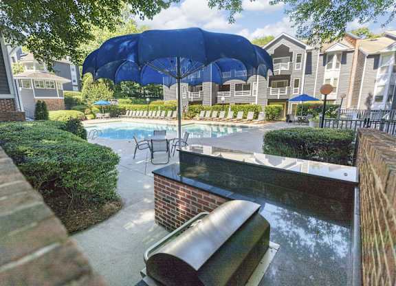 A pool area with a blue umbrella and a brick wall.