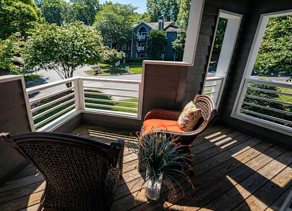 A chair is on a wooden deck with a view of a street and houses.