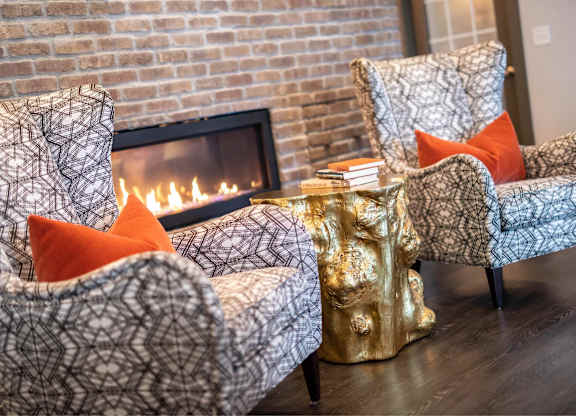 Two chairs with orange pillows in front of a fireplace.