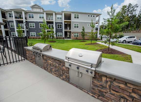A stone wall with a built in grill in front of apartment buildings.