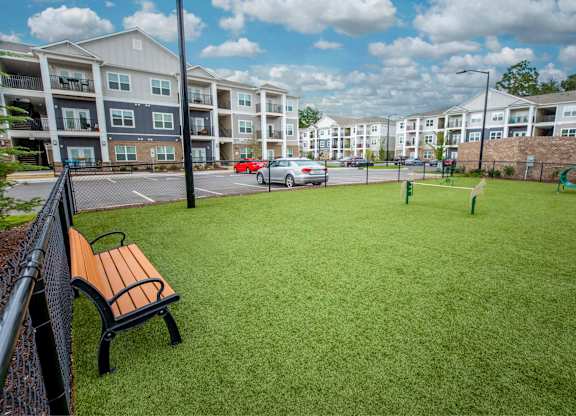 A park area with a bench and a green lawn in front of apartment buildings.
