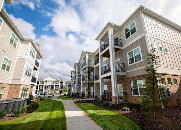 A row of apartment buildings with balconies and a sidewalk in front.