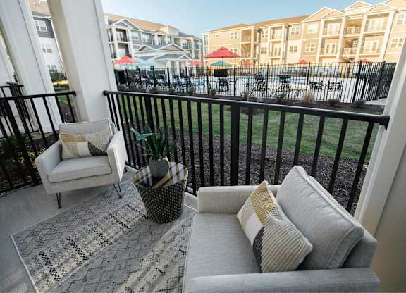 A balcony with a couch, chair, and a potted plant.