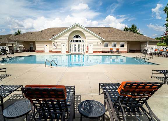 A pool with a building behind it and chairs in front.