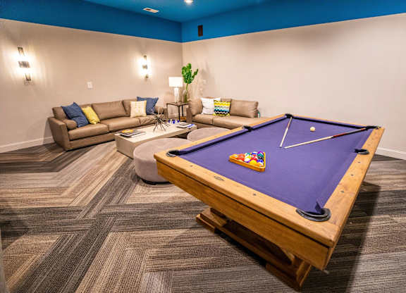 A pool table in a room with a couch and a plant.