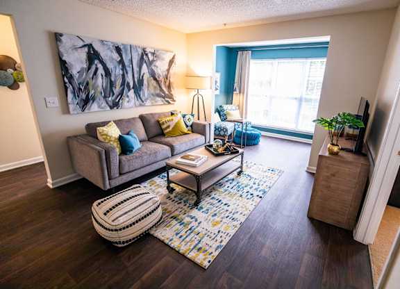 A living room with a grey couch, a coffee table, a rug, and a painting on the wall.