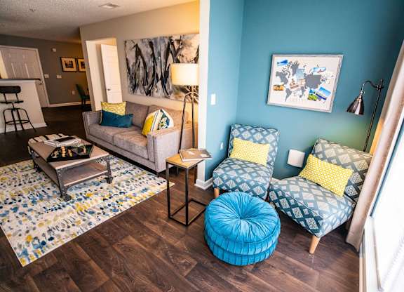 A living room with a grey couch, a blue ottoman, and a yellow pillow.