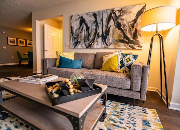 A grey couch with blue and yellow pillows sits in a living room with a large abstract painting above it.