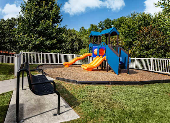 A playground with a blue slide and a black bench.