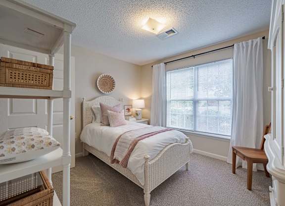 A bedroom with a white bed and a window with white curtains.