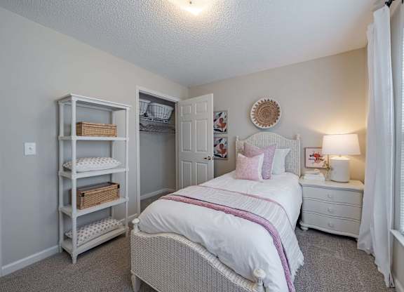 A white bedroom with a bed, nightstand, and a closet with shelves.