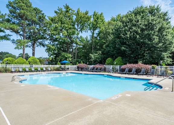 A large outdoor swimming pool surrounded by trees and a fence.