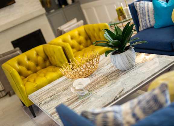 A living room with a yellow sofa and a coffee table with a plant on it.