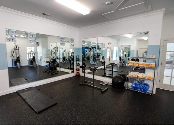 A gym with a mirrored wall and various exercise equipment.
