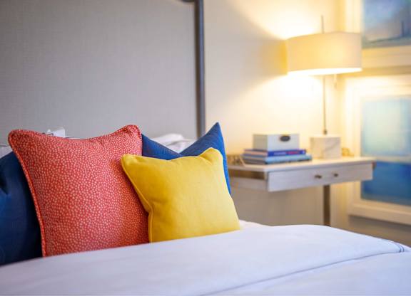 A bed with red and yellow pillows and a white nightstand with a lamp.