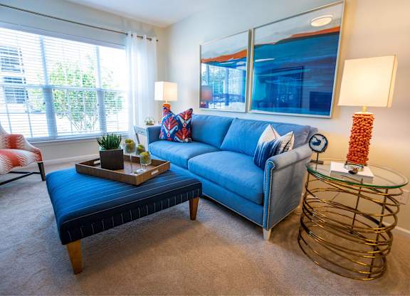 A living room with a blue couch, a wooden coffee table, and a glass side table with a lamp.