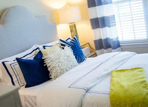 A bed with white sheets and blue and white pillows.