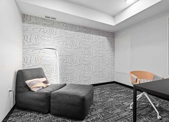 A grey couch with a pillow sits in front of a wallpapered wall.