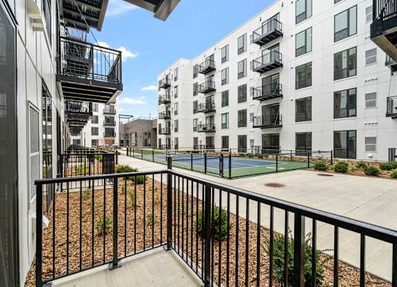 A view of a balcony with a black railing and a tennis court in the background.