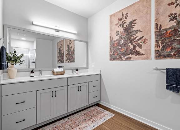 A bathroom with a large mirror, two sinks, and a rug on the floor.