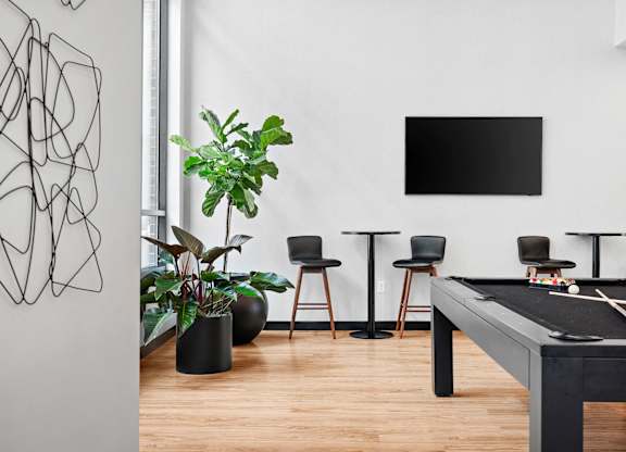 A black pool table is in the middle of a room with a tv and a plant.