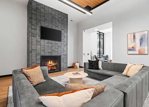 A modern living room with a grey couch, a fireplace, and a painting on the wall.