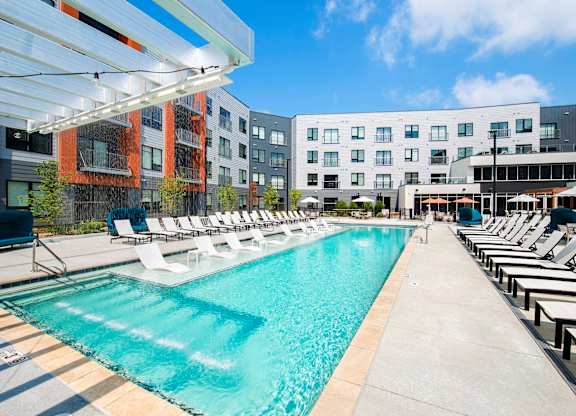 A large swimming pool with lounge chairs and umbrellas in front of a modern building.