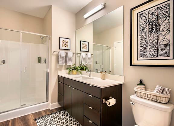 A bathroom with a white toilet, a sink with a mirror, and a shower with a glass door.