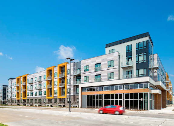A red car is parked in front of a modern building.