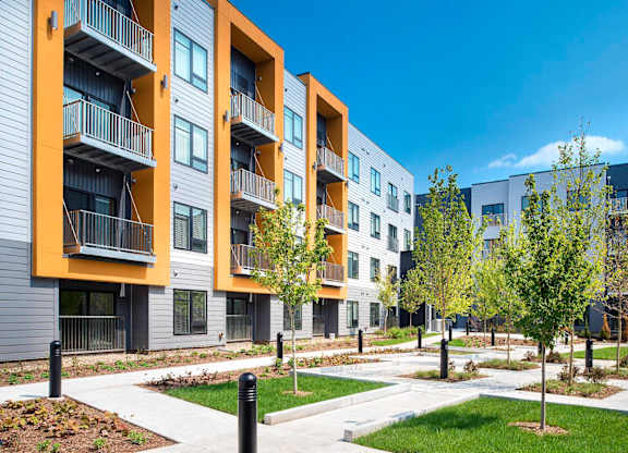 A modern apartment complex with balconies and trees in the foreground.