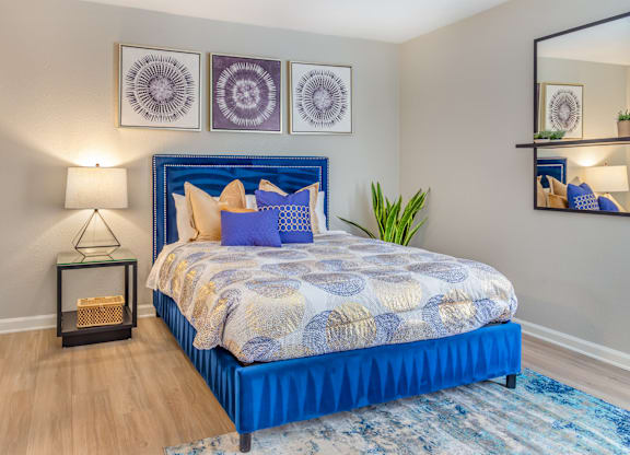 A bedroom with a blue bed and a mirror on the wall.