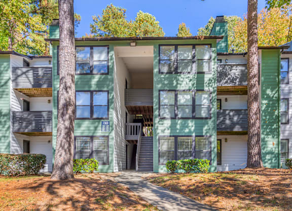 A green and white apartment building with a tree in front.