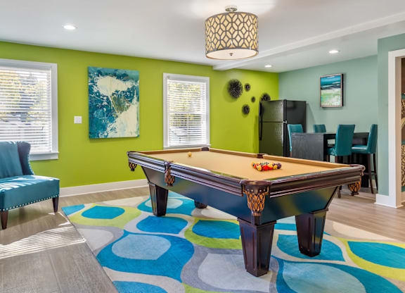 A pool table is in the middle of a room with a blue chair and a green wall.